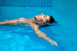 Beautiful Arab woman with arms wide relaxing while floating on her back in swimming pool