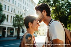 Man kissing woman on forehead standing on the street with sun in the background 5QLMe0