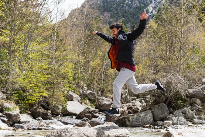 Carefree traveling man jumping over river in mountains