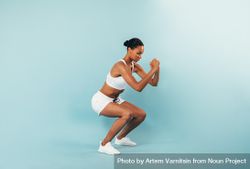 Fit woman in sports bra and shorts squatting in blue studio 5kWNA5