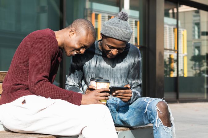 Excited Black friends sharing smartphone on street bench