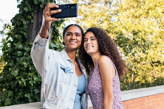 Cheerful women taking selfies with smartphone outdoors