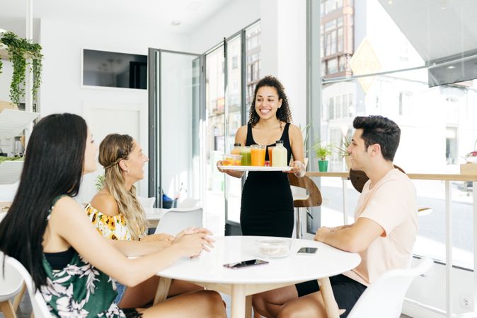 Cheerful waitress serving healthy drinks for friends