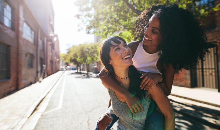 Young woman carrying female friend on back outdoors