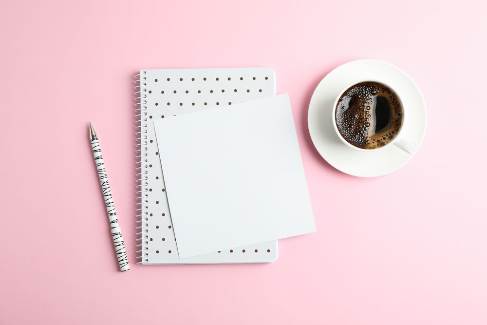 Cup of coffee with copybook and pen on color background, top view