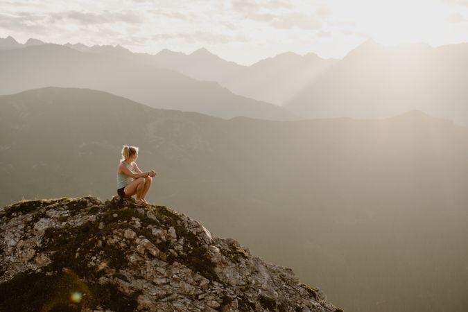 Woman sitting on rock on hill looking at mountains