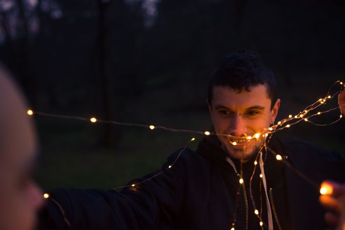 Men unwrapping fairy lights in forest at night