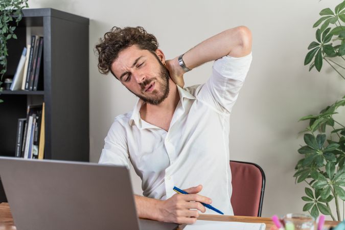 Tired businessman suffering from neck pain while working at his desk.