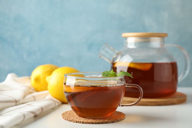 Cup of tea, mint, lemon, tea pot and towel on plain background, copy space