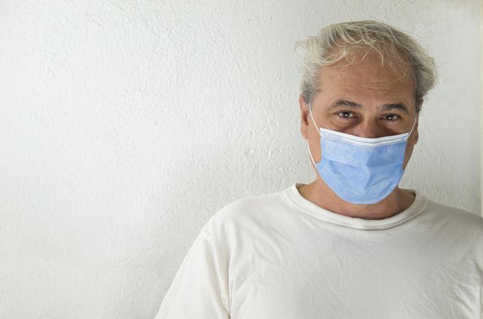 Portrait of middle aged man in light shirt wearing facemask against light wall