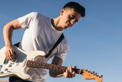 man playing electric guitar on a blue sky background