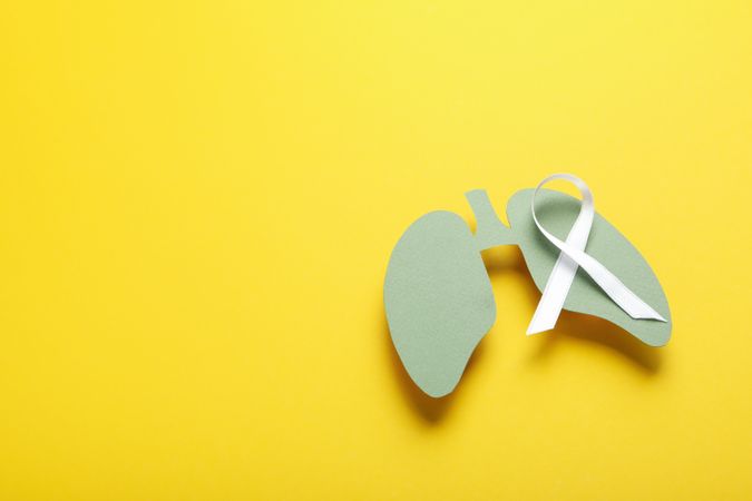 Green lungs cut out of paper with ribbon on yellow background with copy space