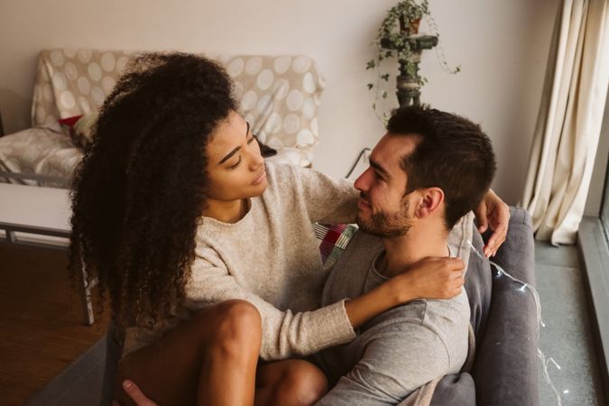 Young multiracial couple hugging on sofa