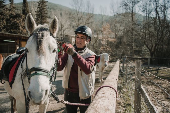 Older man putting bridle on horse