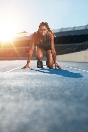 Young female sprinter taking ready to start position facing the camera