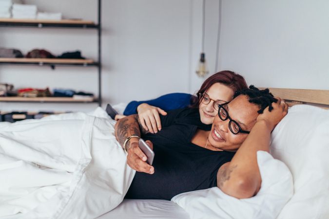 Happy couple lying on a bed in a bedroom and watching mobile phone