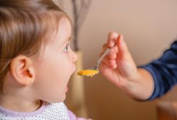 Baby eating puree from a spoon in the hand of mother