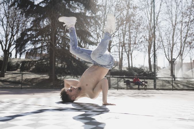 Shirtless man dancing break dance in park