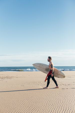Man in wetsuit walking along the coast with surfboard, vertical