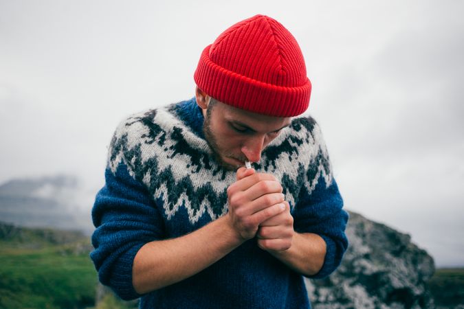 Man in woolen sweater lighting cigarette on overcast day