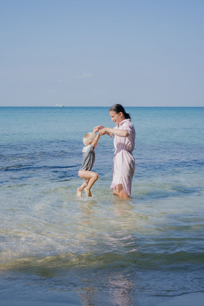 Woman and small kid having fun with water while relaxing on seacoast at resort