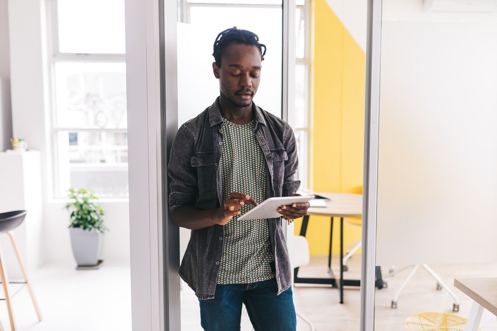 Young man using a tablet while standing in a bright, open  office