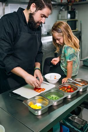 Chef teaching little girl how to prepare healthy poke bowl in a professional kitchen