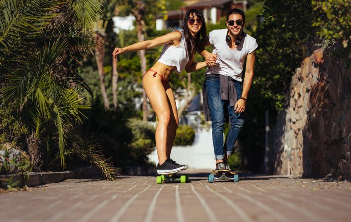 Happy couple riding on skateboards on walkway