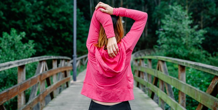 Unrecognizable sportswoman doing stretching arms outdoors