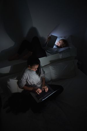 Woman and boy surfing gadgets in dark room at home