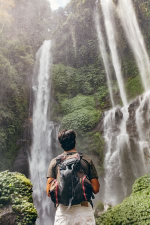 Male hiker looking at waterfall in forest