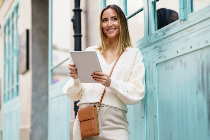 Chic woman in cream standing outside with digital tablet