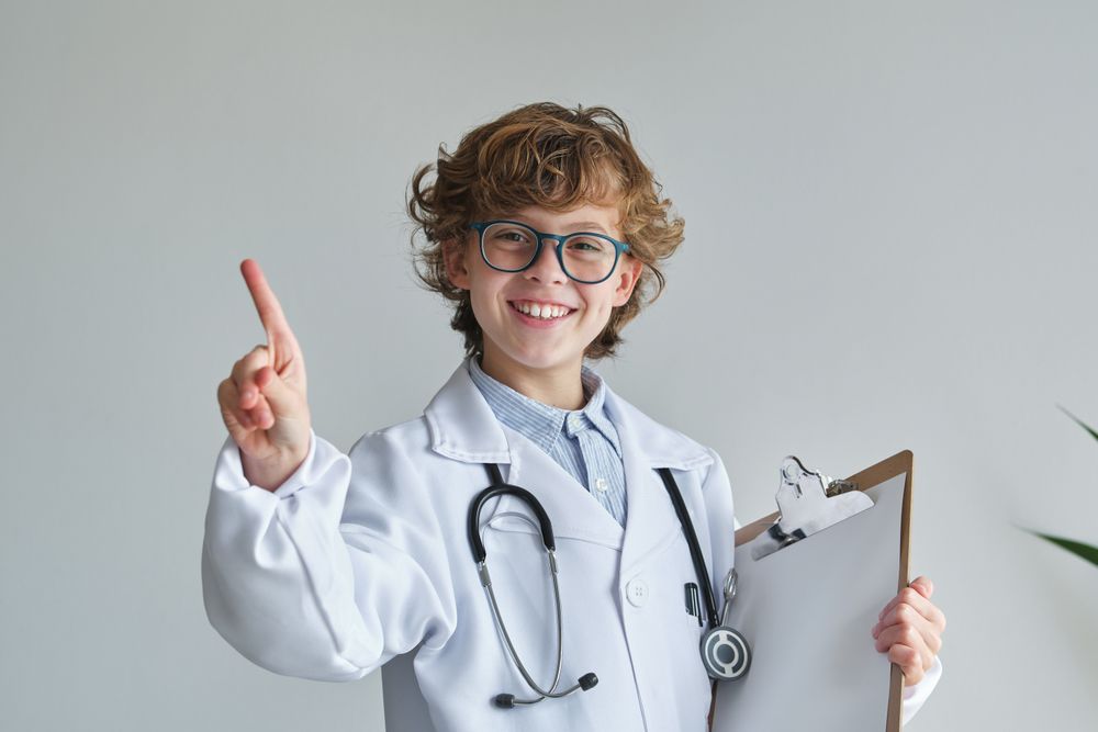 Cheerful boy in medical robe with finger up