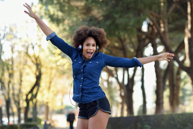 Female in denim shirt with open arms in front of trees