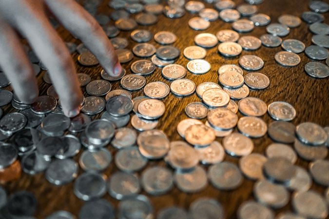 A hand over a table scattered with coins