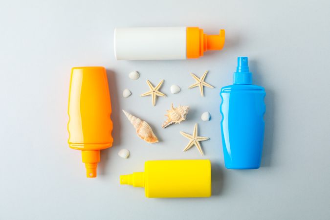 Flat lay composition with sunscreen sprays and starfishes on color background, space for text. Summer vacation backdrop