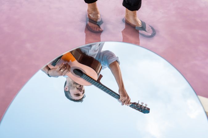 Reflection of inspired musician playing guitar at seashore in mirror