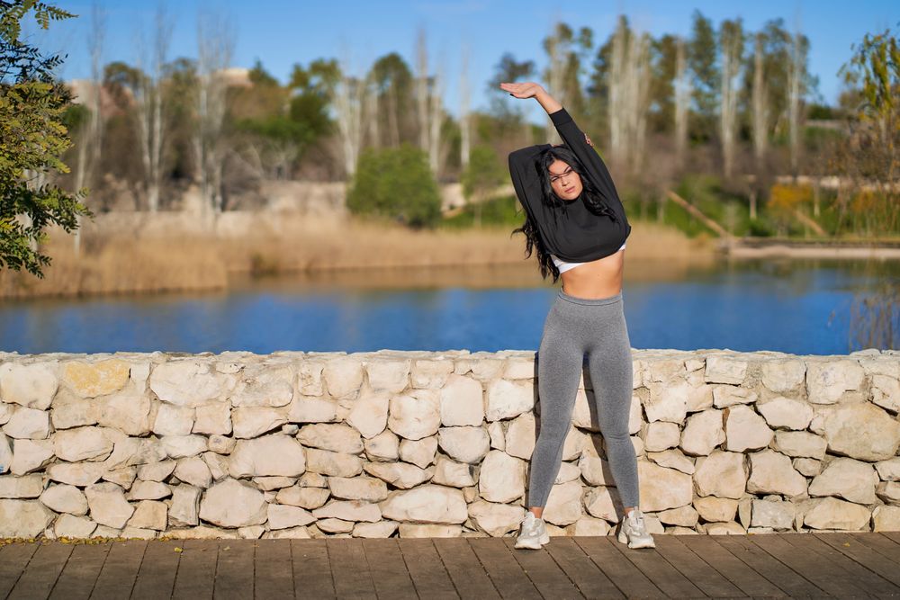 a young female athlete stretches on a rock wall next to a lake