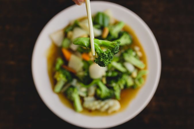 Hand holding broccoli with chopsticks over vegetarian soup