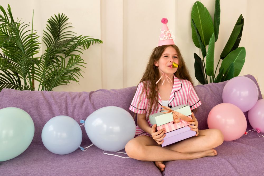Young girl celebrating her birthday at home, holding presents.