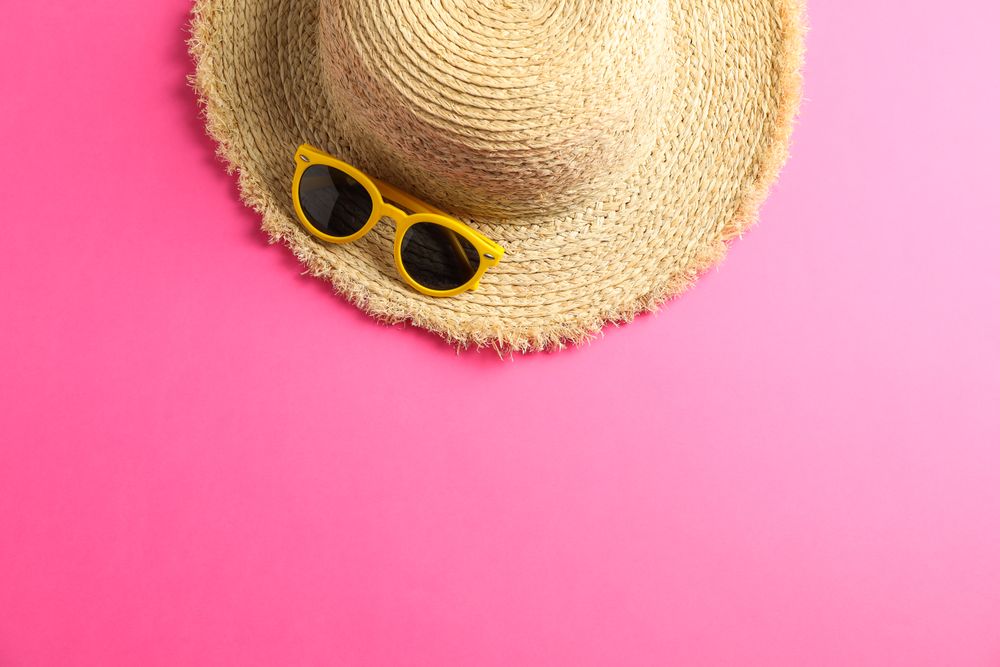 Straw hat with sunglasses on color background, space for text, top view. Summer backdrop