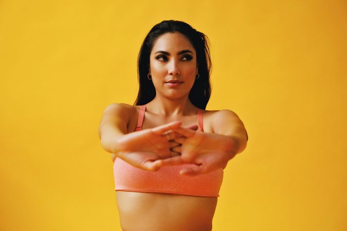 Hispanic female sitting in yoga pose stretching her arms in front of her in yellow studio shoot