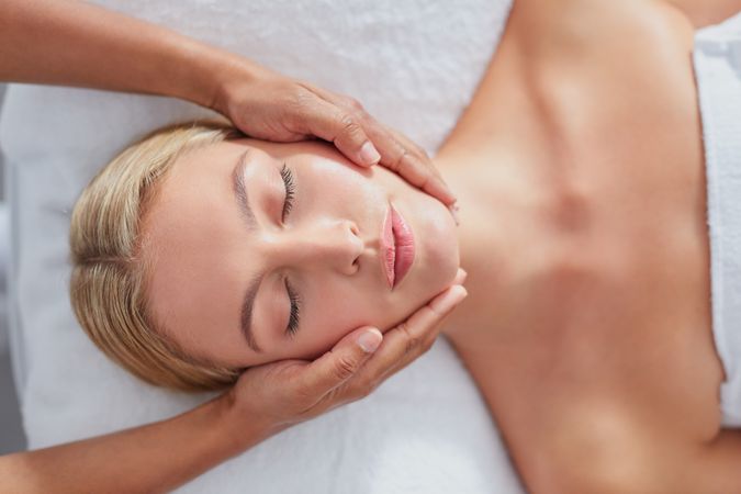 Face of blonde woman lying back and relaxing during facial treatment