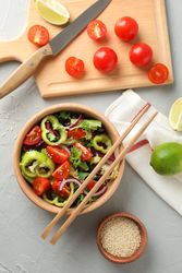Fresh salad with chopsticks and kitchen accessories on grey background, top view