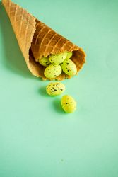 Waffle cone with small speckled eggs on green pastel background