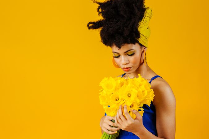 Portrait of sad Black woman with large earrings holding a bouquet of daffodils