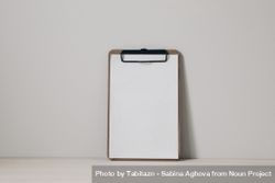 Wooden clipboard mockup with blank paper sheet on a wooden table against neutral beige wall background 4MXEa5