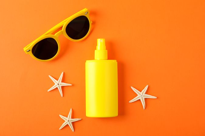 Composition with sunscreen spray, starfishes and sunglasses on color background, space for text. Summer backdrop