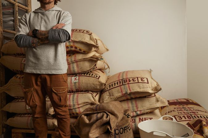 Tattooed barista stands proudly in front of big bags with imported raw coffee beans