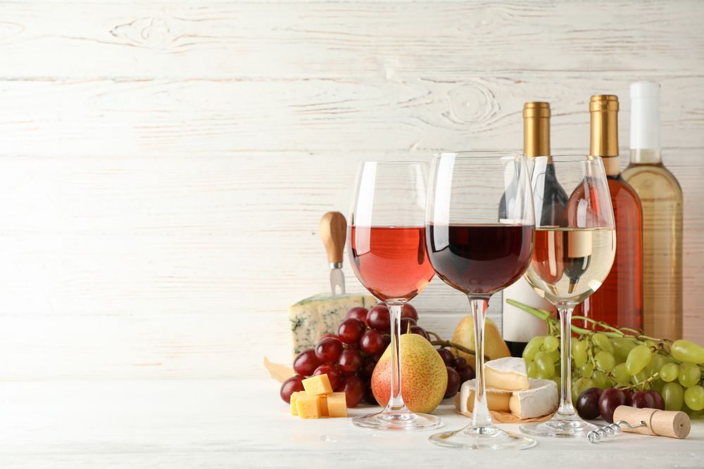 Fruits, cheese, bottles and glasses with different wine on light background, space for text
